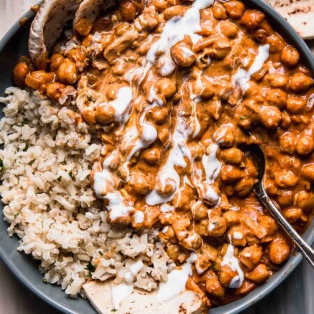 Overhead shot of butter chickpeas served on bed of brown rice in grey bowl with pita bread.