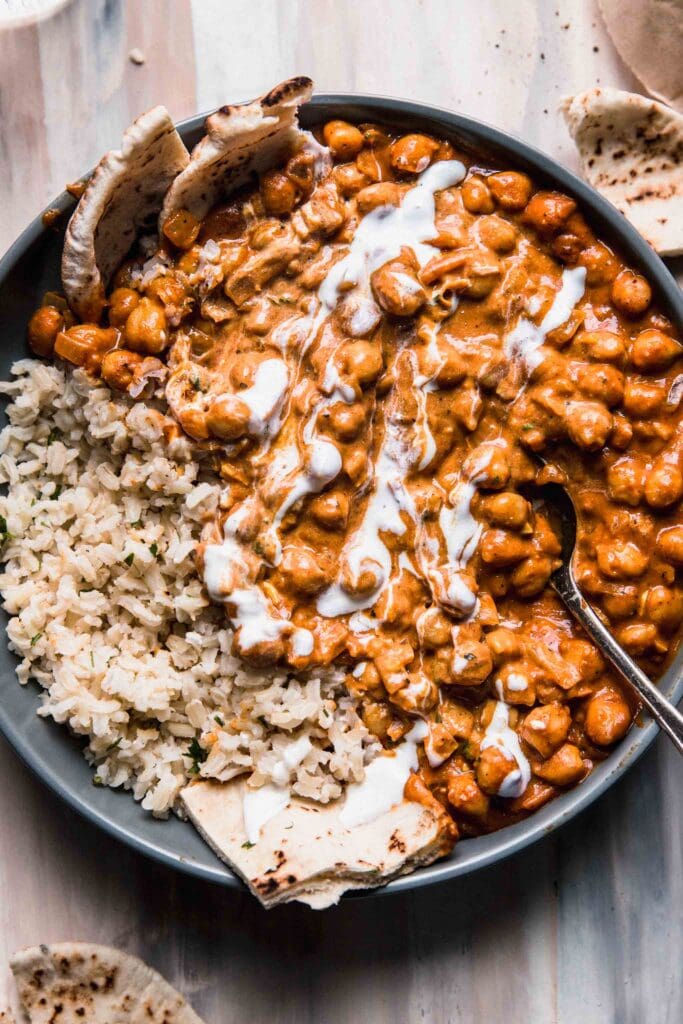 Overhead shot of butter chickpeas served on bed of brown rice in grey bowl with pita bread.
