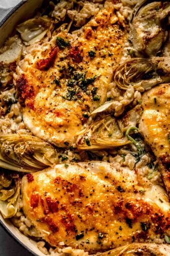 Overhead closeup of spinach and artichoke orzo in skillet topped with chicken.
