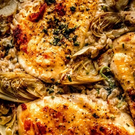 Overhead closeup of spinach and artichoke orzo in skillet topped with chicken.