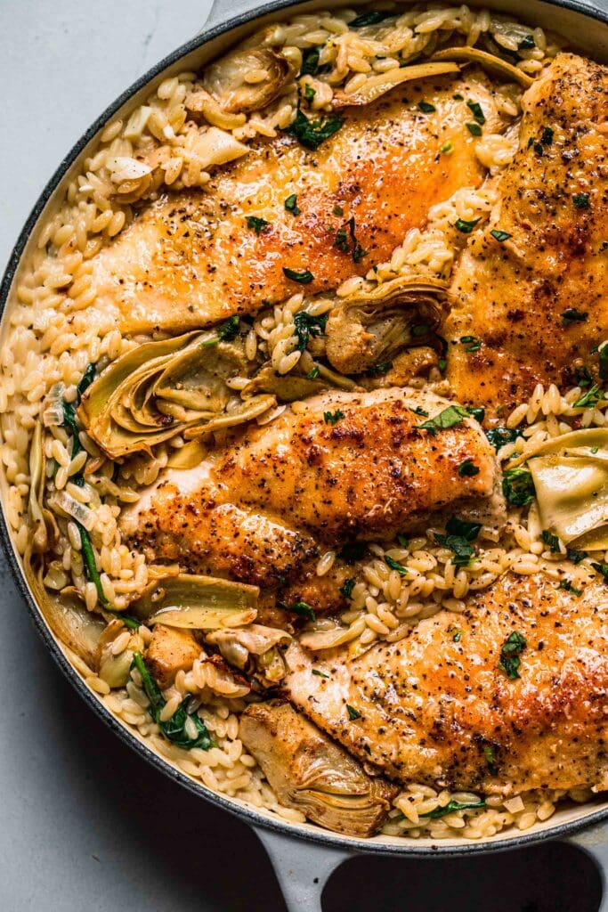 Overhead close up shot of spinach artichoke orzo with chicken in skillet.