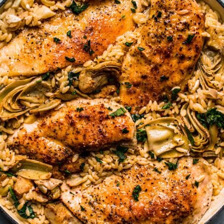 Overhead shot of spinach artichoke orzo with chicken in skillet.