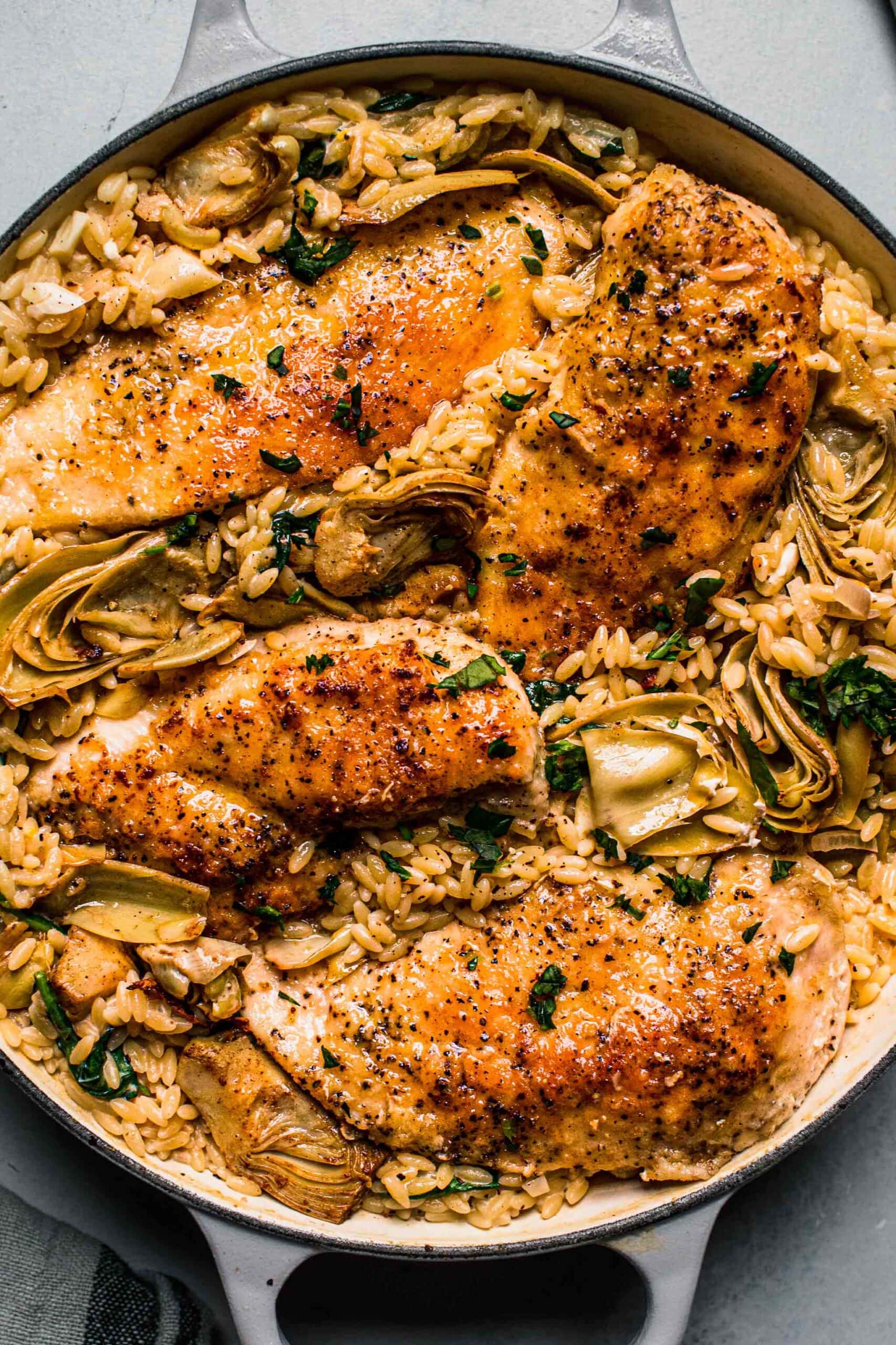 Overhead shot of spinach artichoke orzo with chicken in skillet.