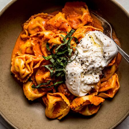 Overhead shot of creamy tortellini in bowl topped with burrata cheese.