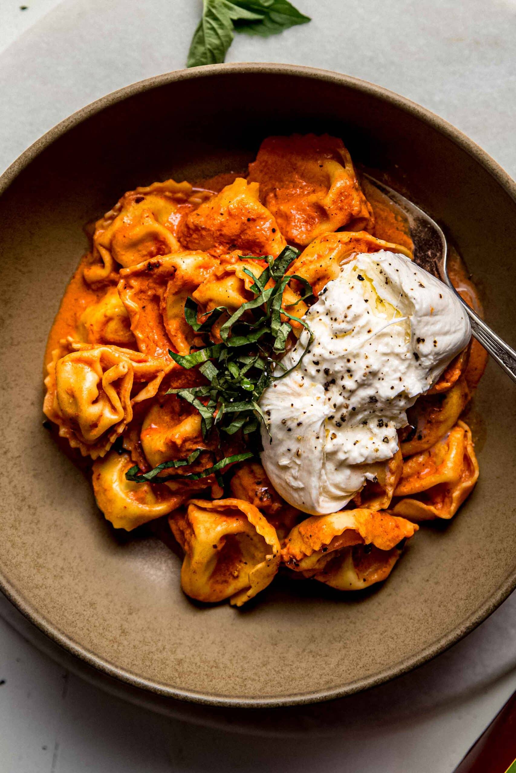 Overhead shot of creamy tortellini in bowl topped with burrata cheese.