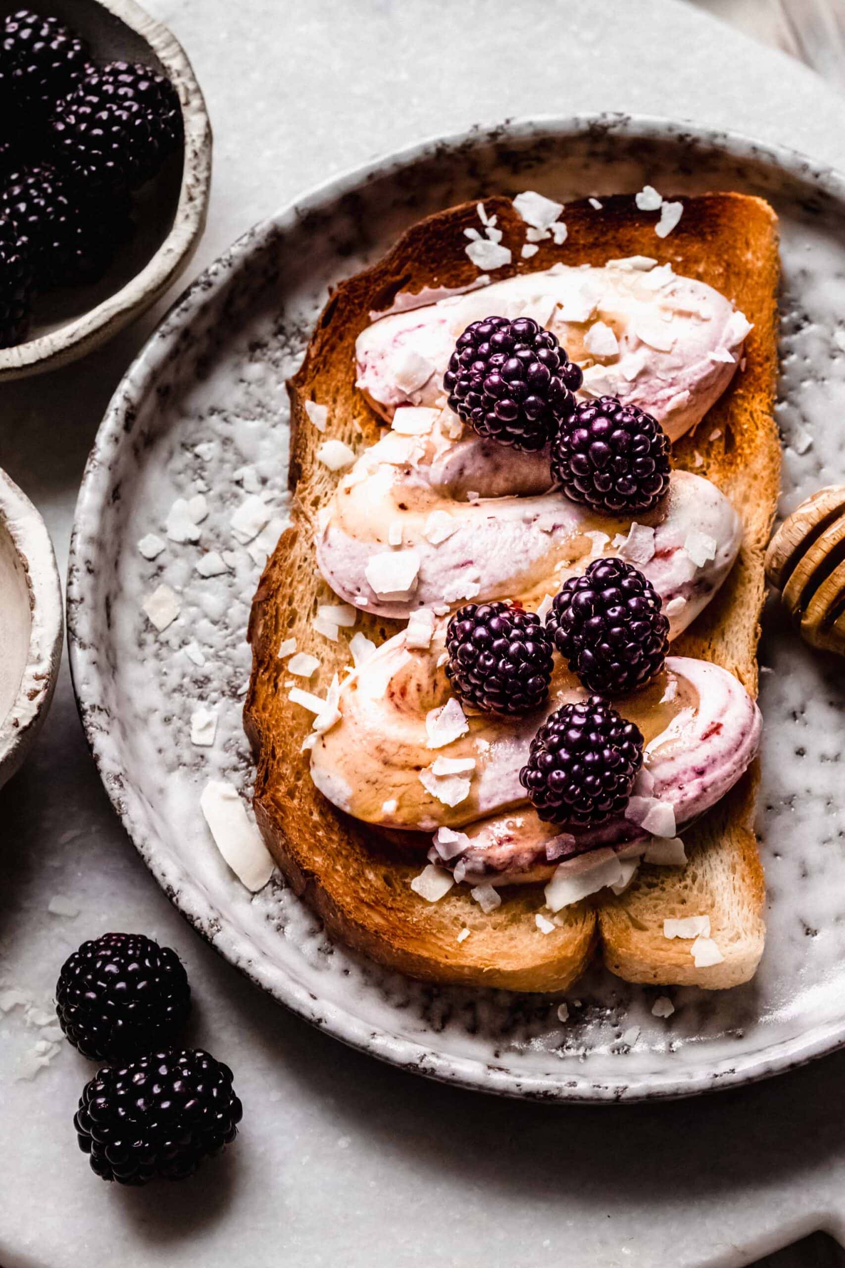 Toast on grey plate with swirl of ricotta cheese, drizzle of honey and blackberries.