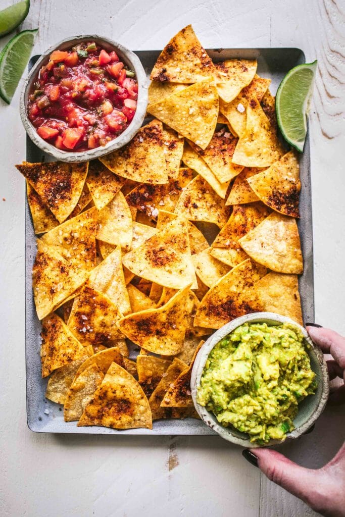Baked tortilla chips on tray with salsa and guacamole. 