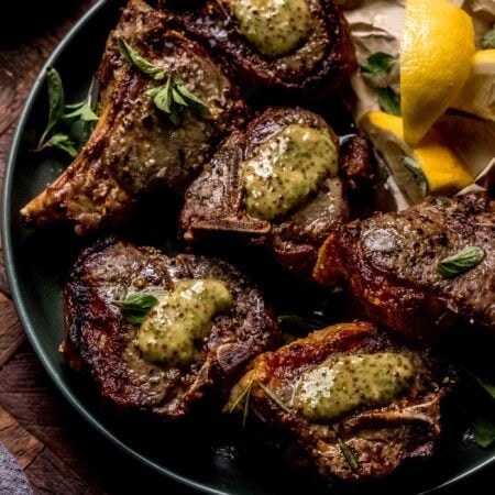 Lamb chops on plate with dollops of mint mustard sauce on top of them.