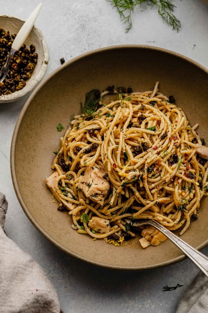 Small bowl of capers next to bowl of tuna pasta. 