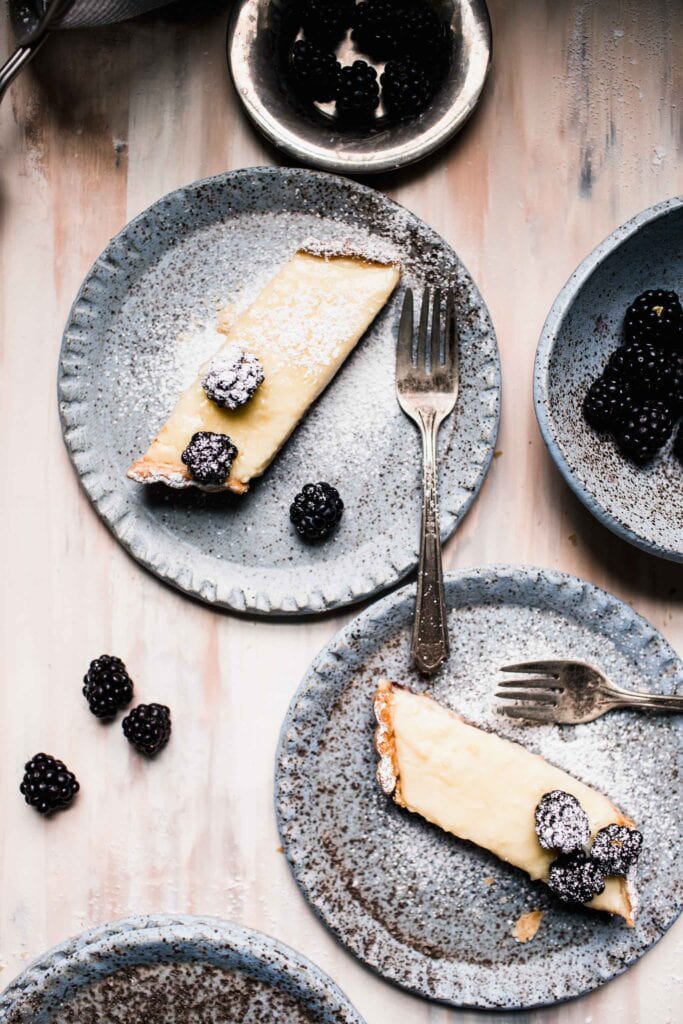 Overhead shot of two slices on custard tart on plates next to bowl of blackberries. 