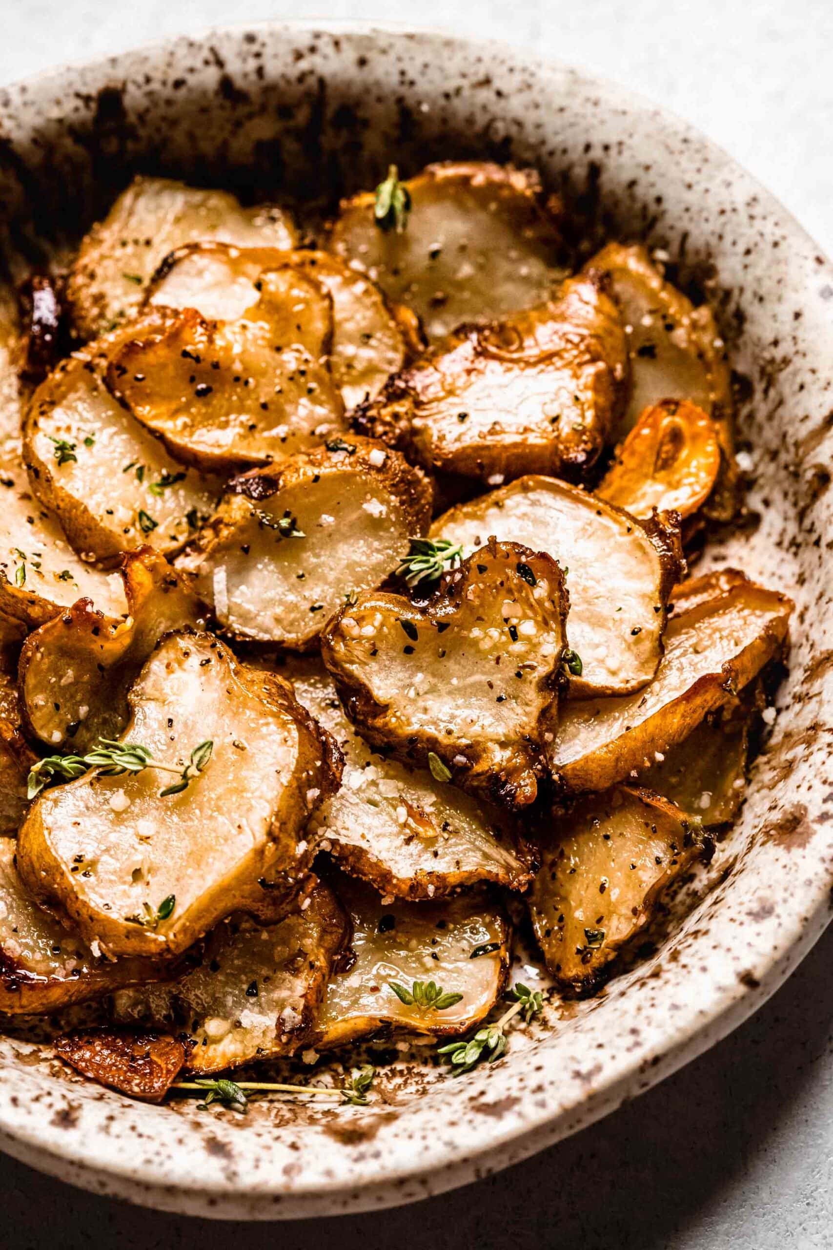 Roasted sunchokes in brown speckled bowl.