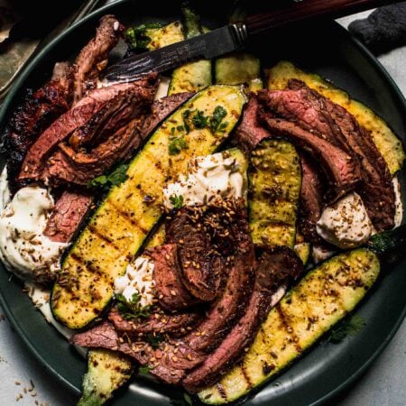 Slices of grilled steak on green plate with zucchini and feta scattered around.