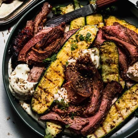 SLICED FLANK STEAK ARRANGED ON PLATE WITH DOLLOPS OF WHIPPED FETA AND SLICES OF GRILLED ZUCCHINI.