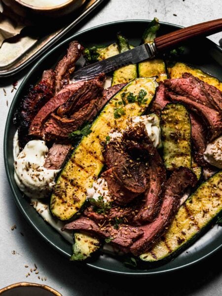 SLICED FLANK STEAK ARRANGED ON PLATE WITH DOLLOPS OF WHIPPED FETA AND SLICES OF GRILLED ZUCCHINI.