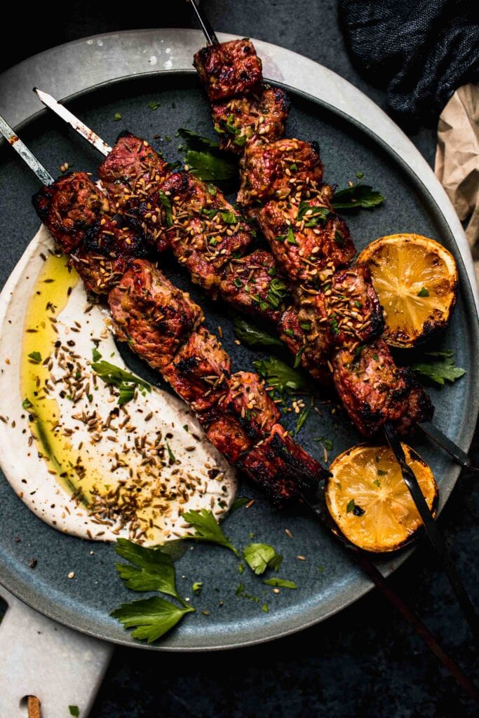 Overhead view of grilled lamb kebabs on grey plate.