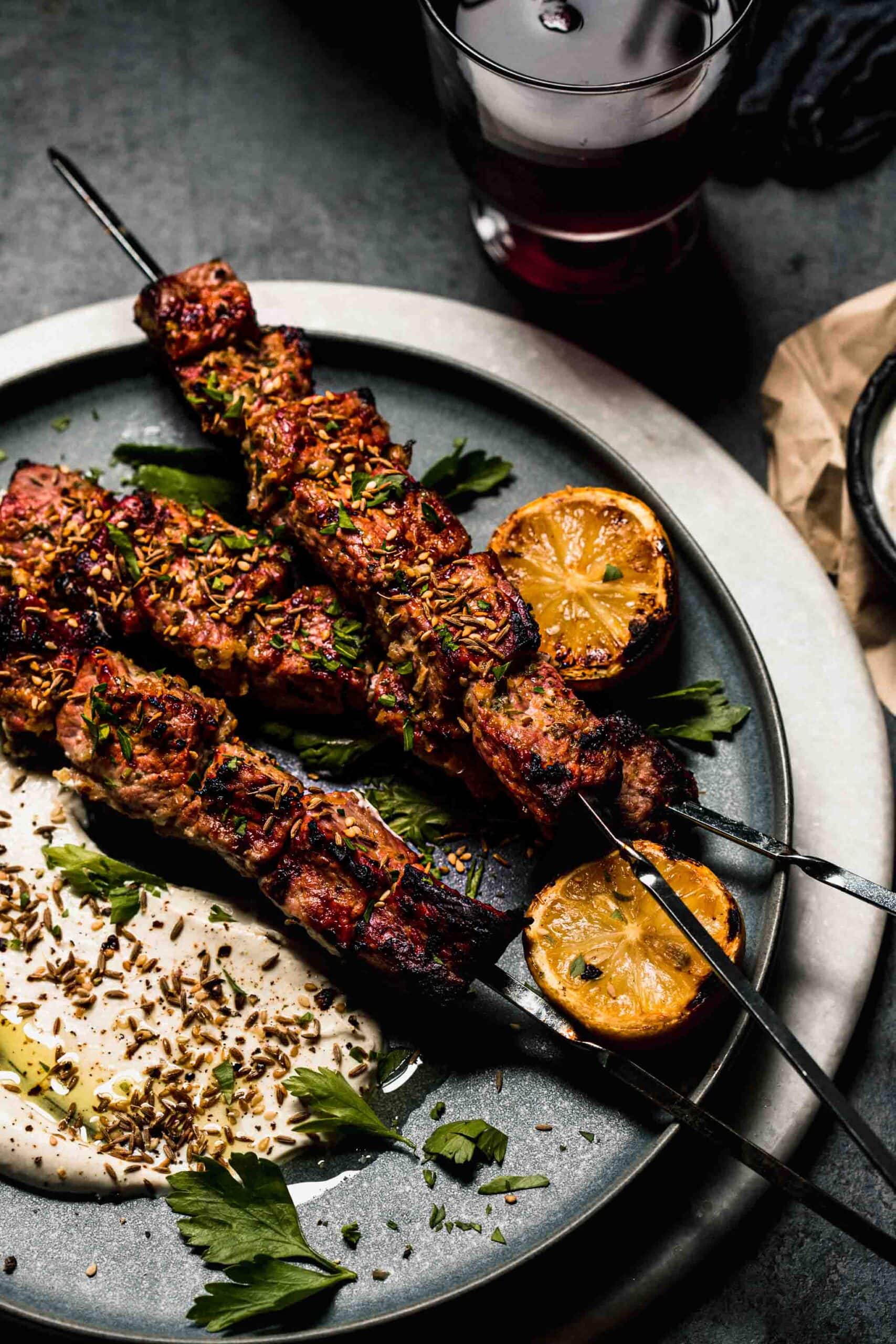 Side view of grilled lamb kebabs on grey plate.