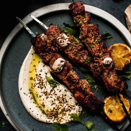 Grilled lamb kebabs on plate with dollops of sesame sauce.
