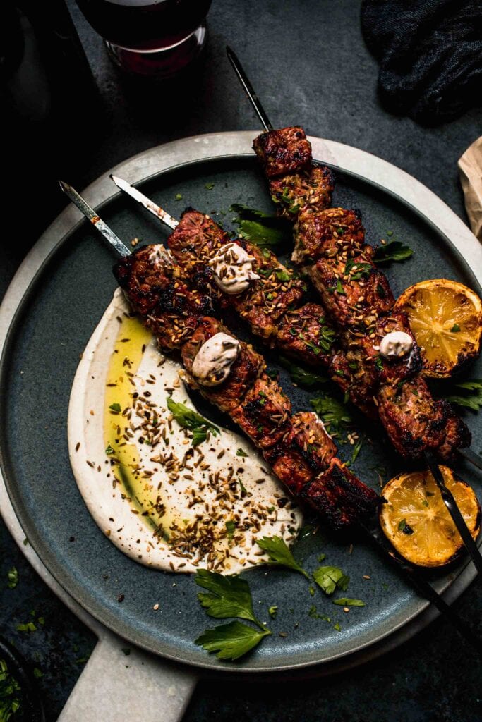 Grilled lamb kebabs on plate with dollops of sesame sauce.