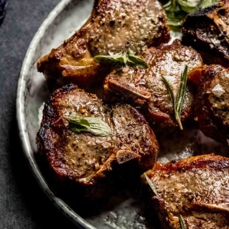 Lamb chops arranged on grey plate topped with mint leaves.