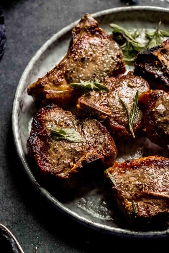 Lamb chops arranged on grey plate topped with mint leaves.
