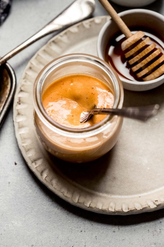 Small jar of sauce with spoon next to honey wand. 