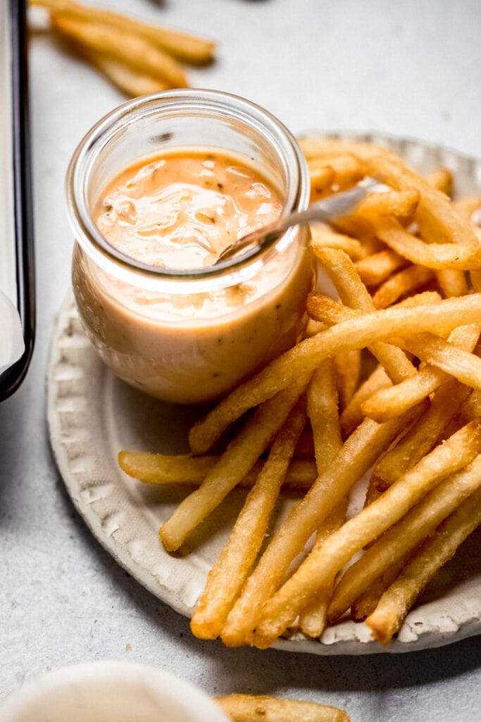 Side view of in-n-out sauce with spoon surrounded by fries.