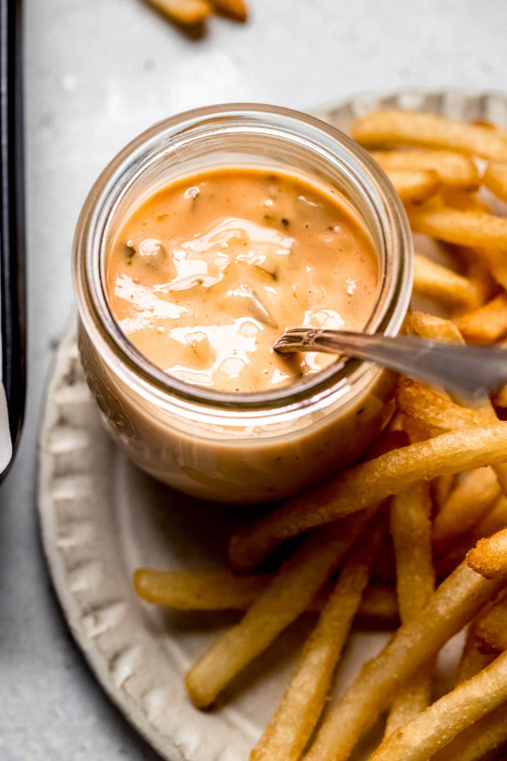 Bowl of in-n-out sauce with spoon surrounded by fries.