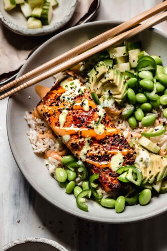 Piece of salmon on top of rice drizzled with wasaba and sriracha mayo.
