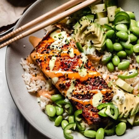 Piece of salmon on top of rice drizzled with wasaba and sriracha mayo.