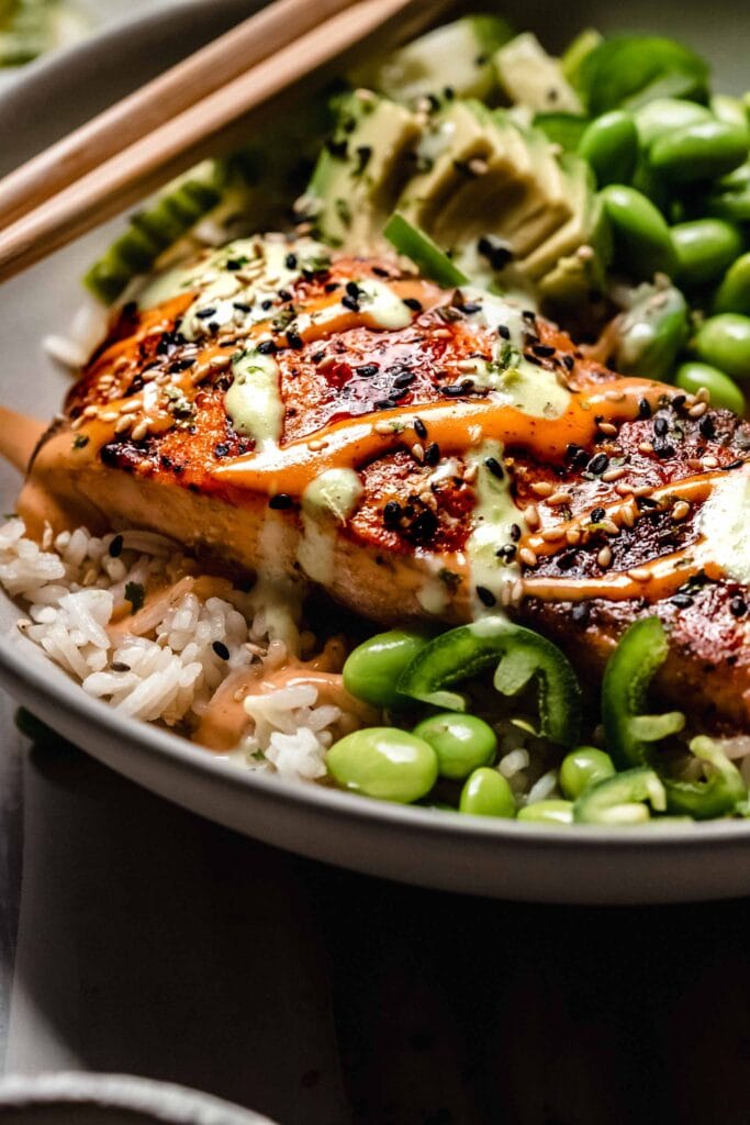 Side view of salmon topped sushi bowl with chopsticks.