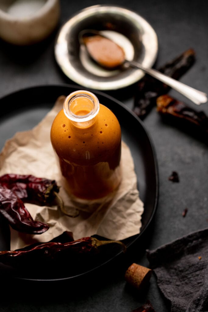 Overhead shot of bottle of salsa taquera next to dried chiles and spoon with sauce.