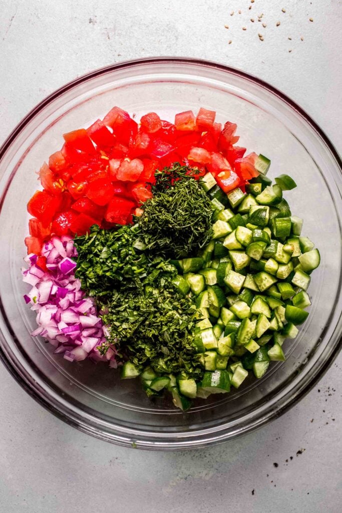 Chopped veggies and fresh herbs in bowl before tossing. 
