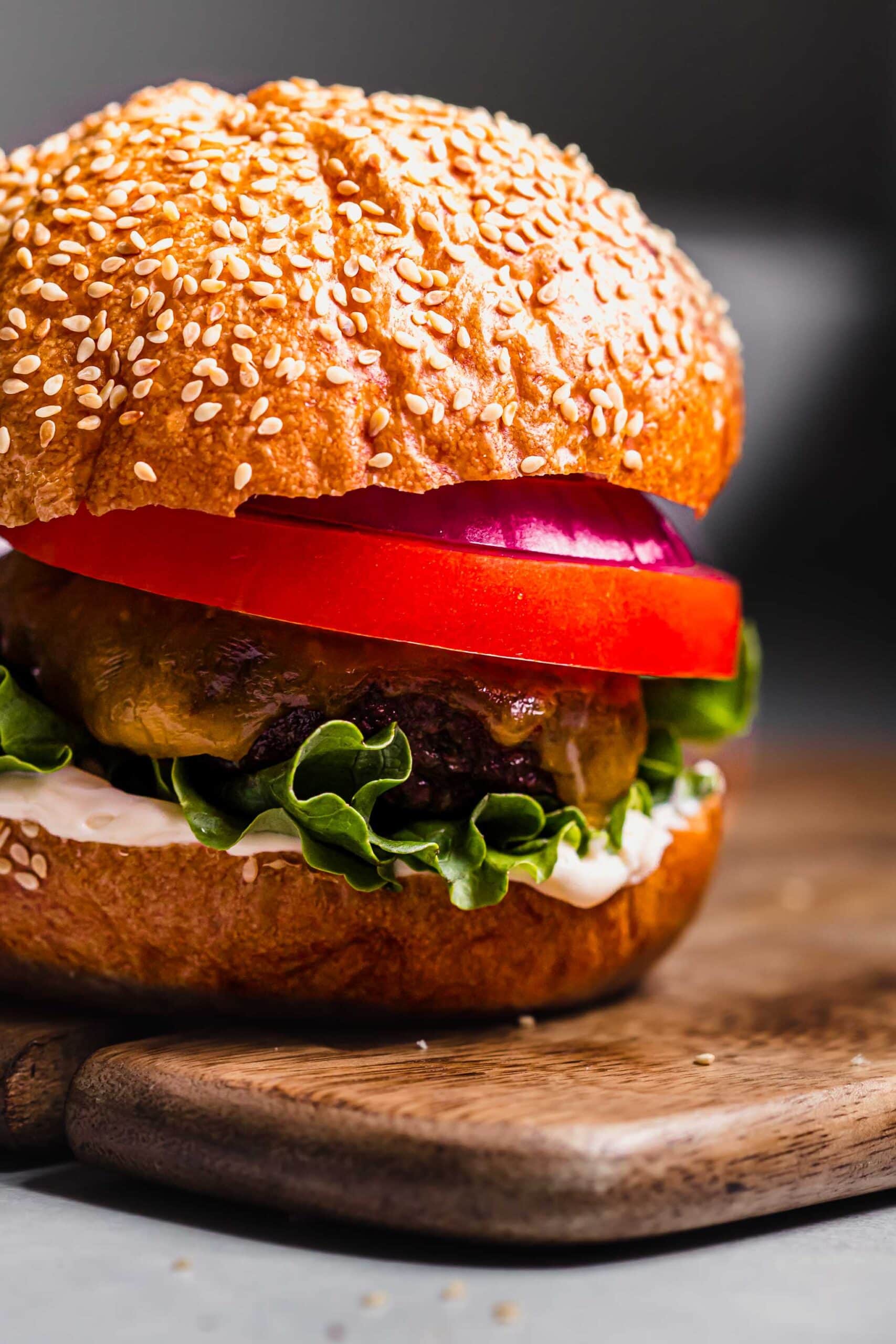 Side view close up of burger topped with tomato, lettuce and red onion.