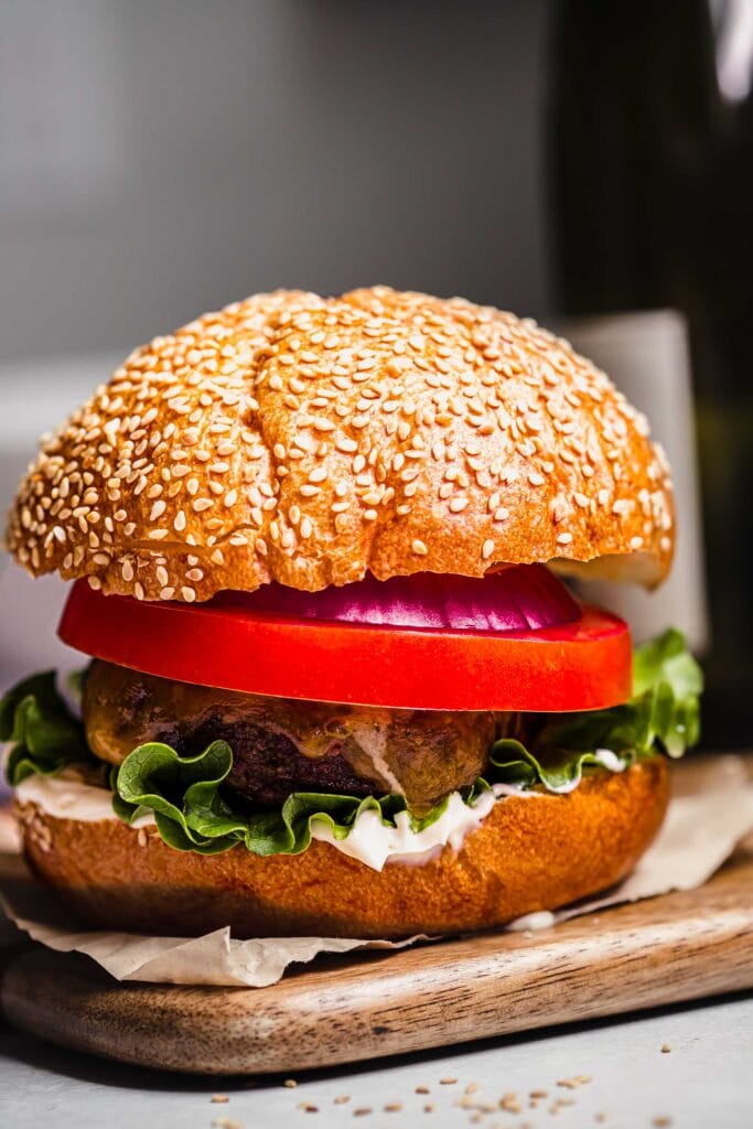 Side view of burger topped with tomato, lettuce and red onion.