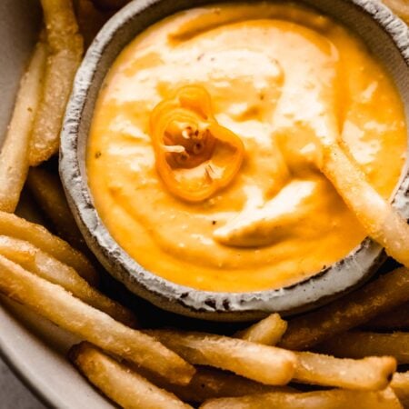 Small bowl of aji amarillo sauce topped with habanero pepper and surrounded by french fries.