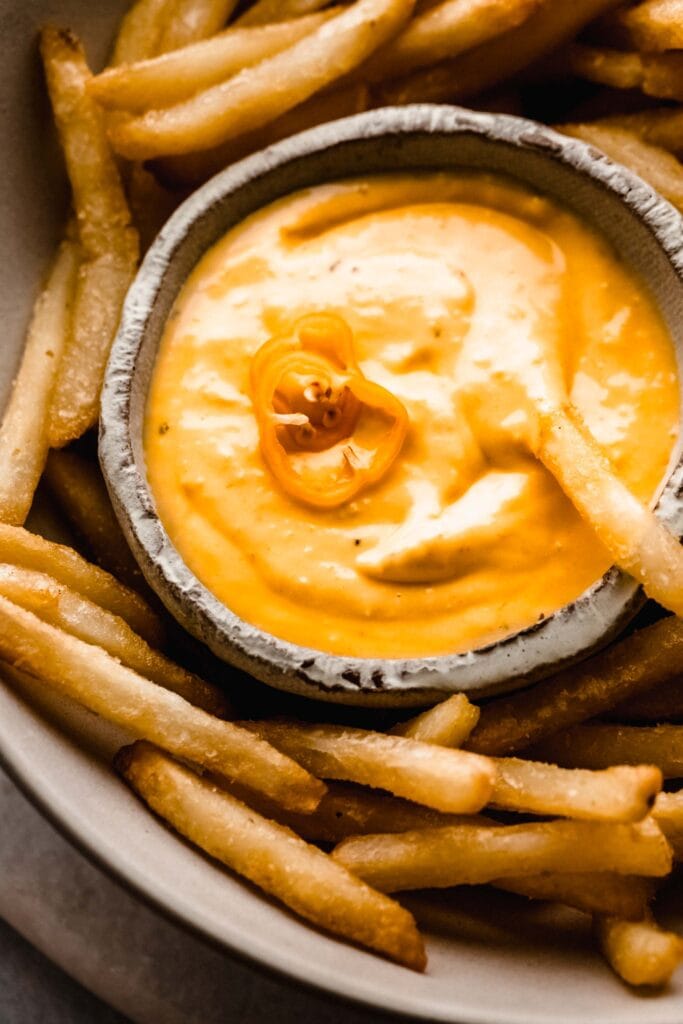 Small bowl of aji amarillo sauce topped with habanero pepper and surrounded by french fries.