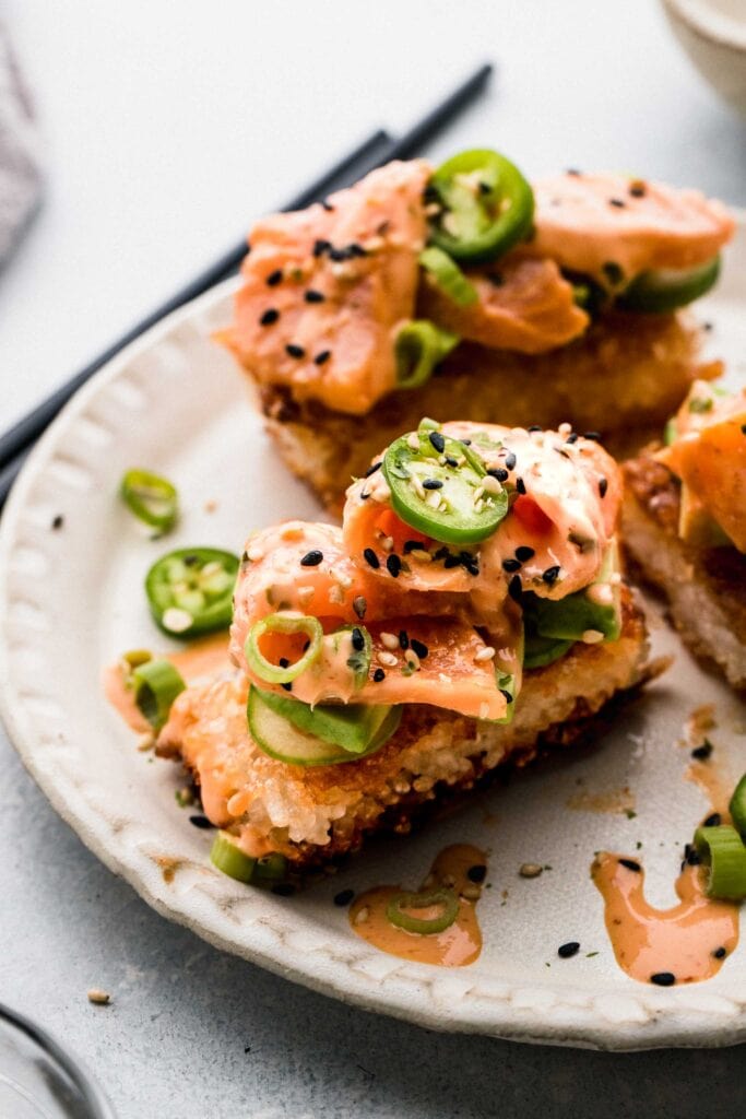 Crispy rice bites arranged on plate topped with spicy salmon. 