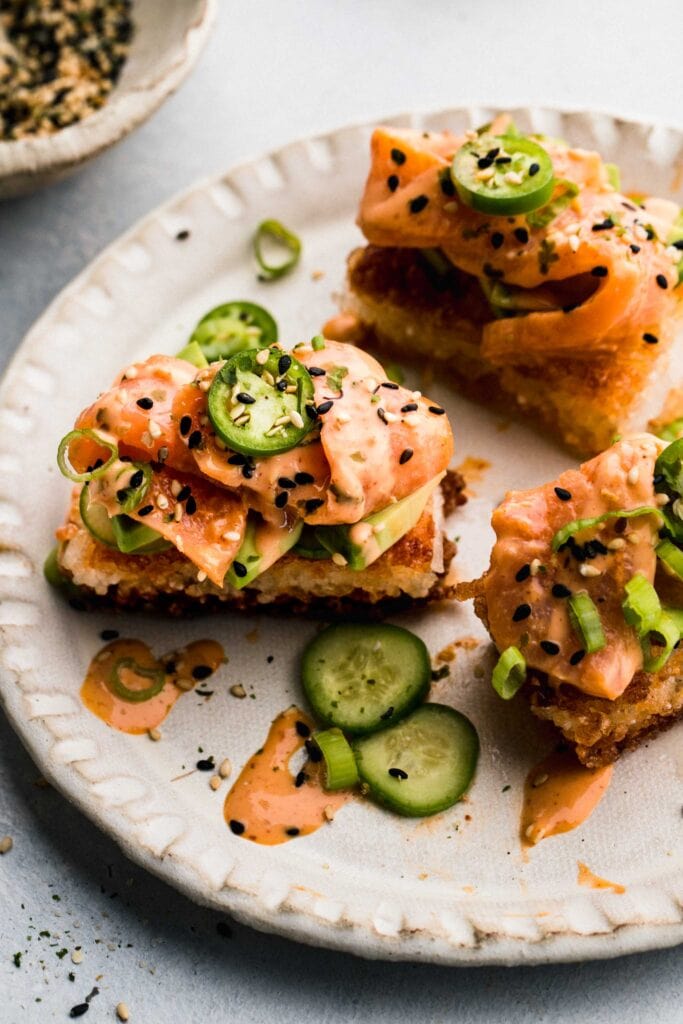 3 crispy rice sushi bites on plate topped with creamy sauce and spicy peppers.