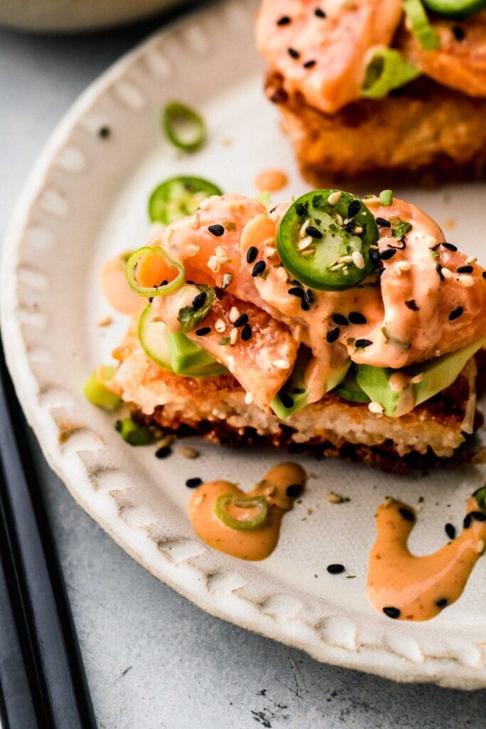 Side view of crispy rice sushi bite on plate drizzled with creamy sriracha.