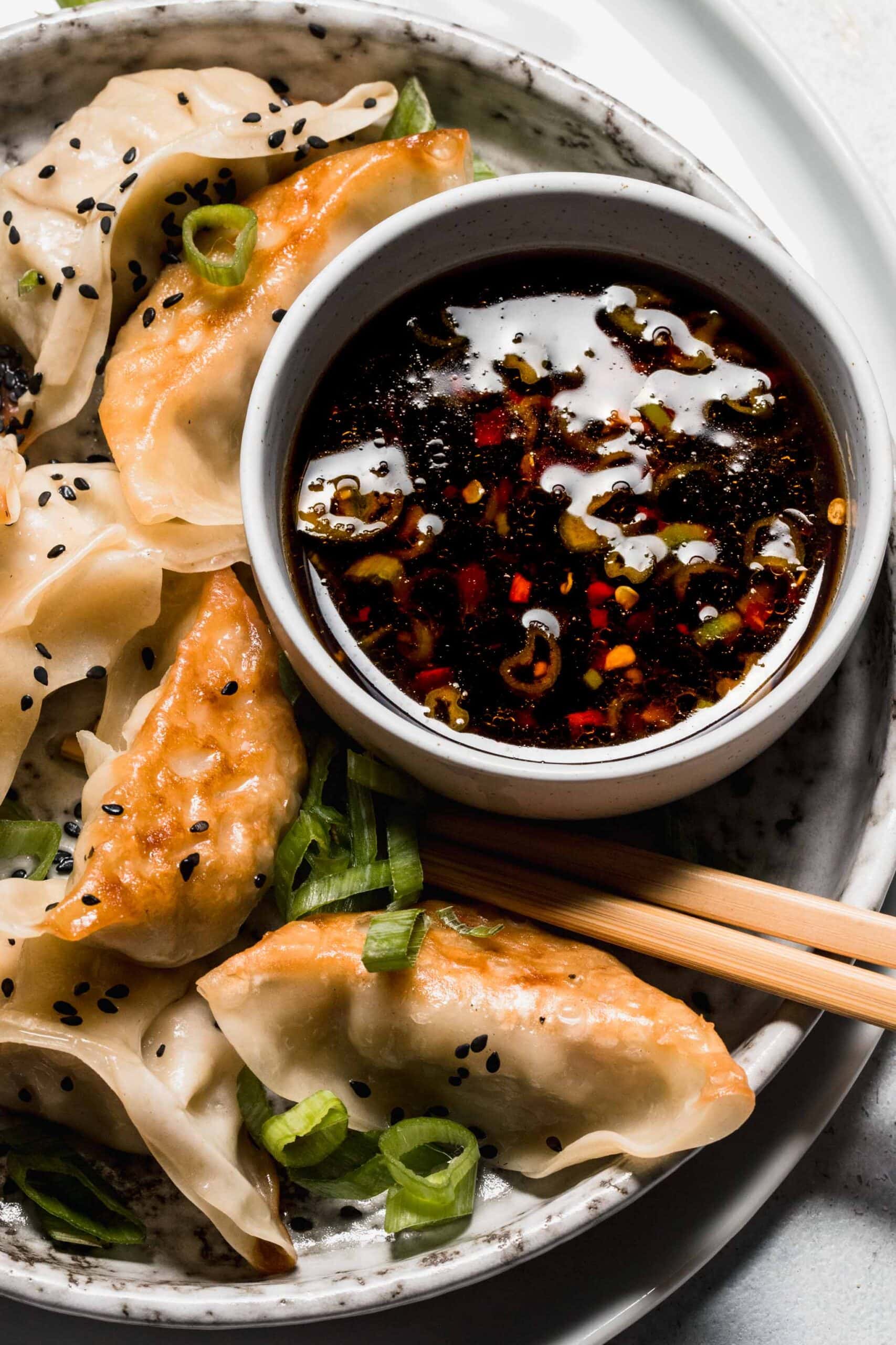 Bowl of gyoza sauce on plate of potstickers.