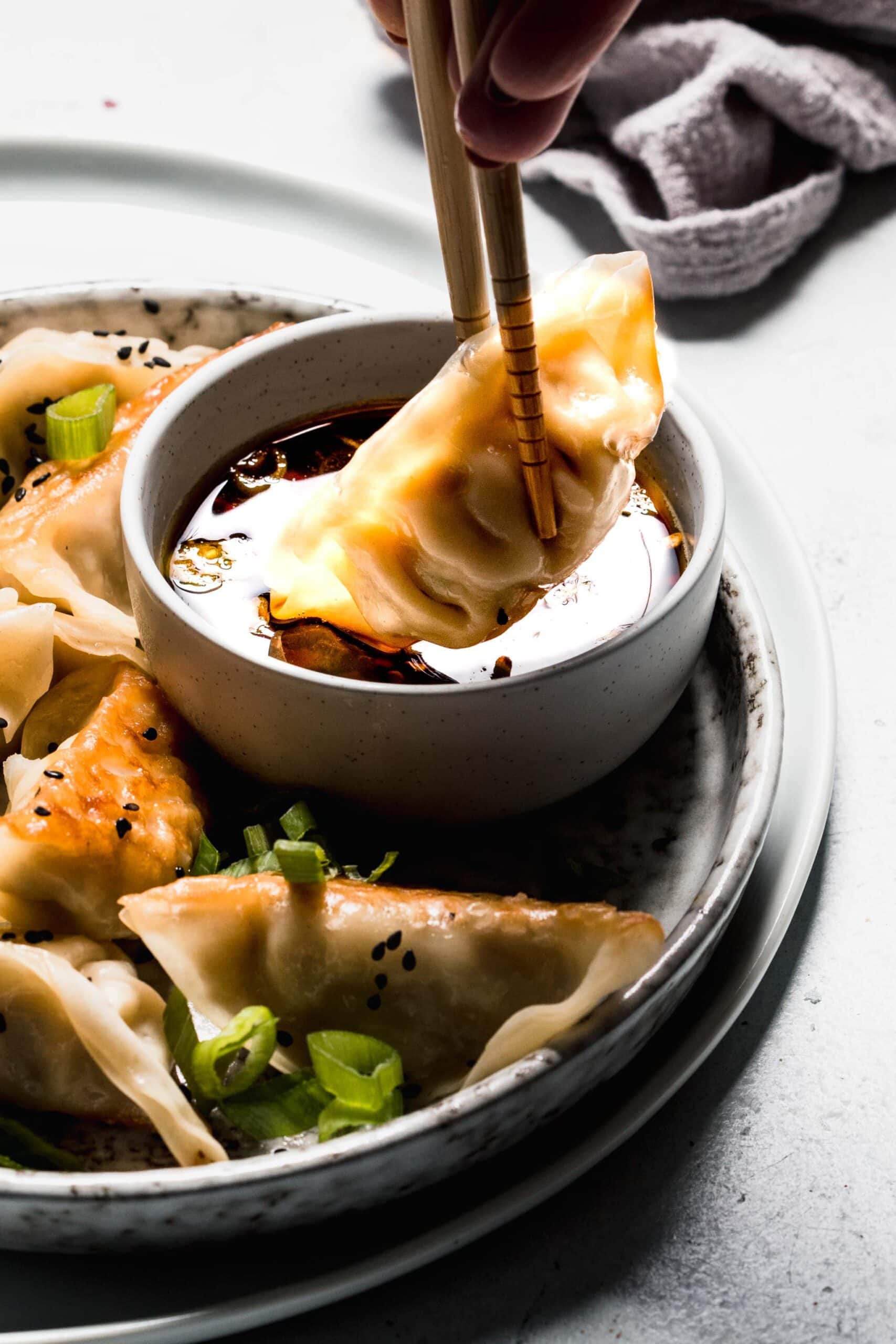 Chopsticks dipping gyoza into sauce.