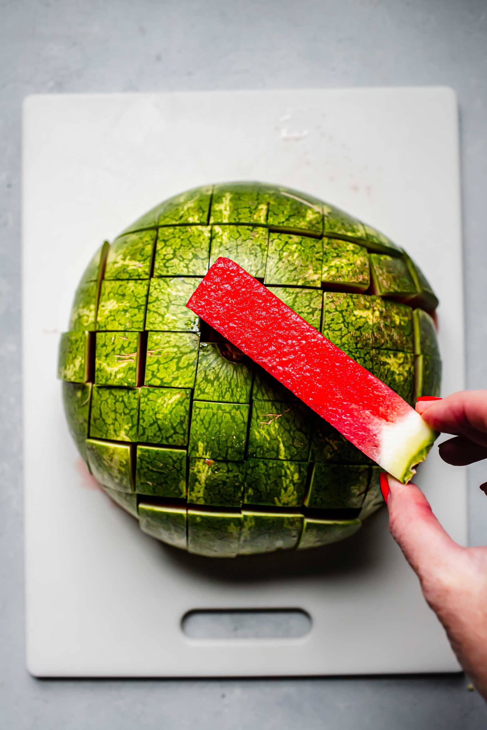 Hand holding stick of watermelon next to cut up melon.