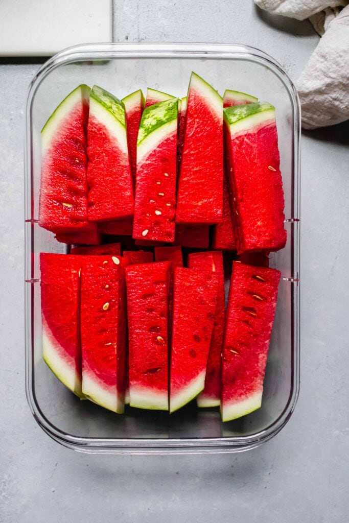 Watermelon sticks stacked in large tuperware.