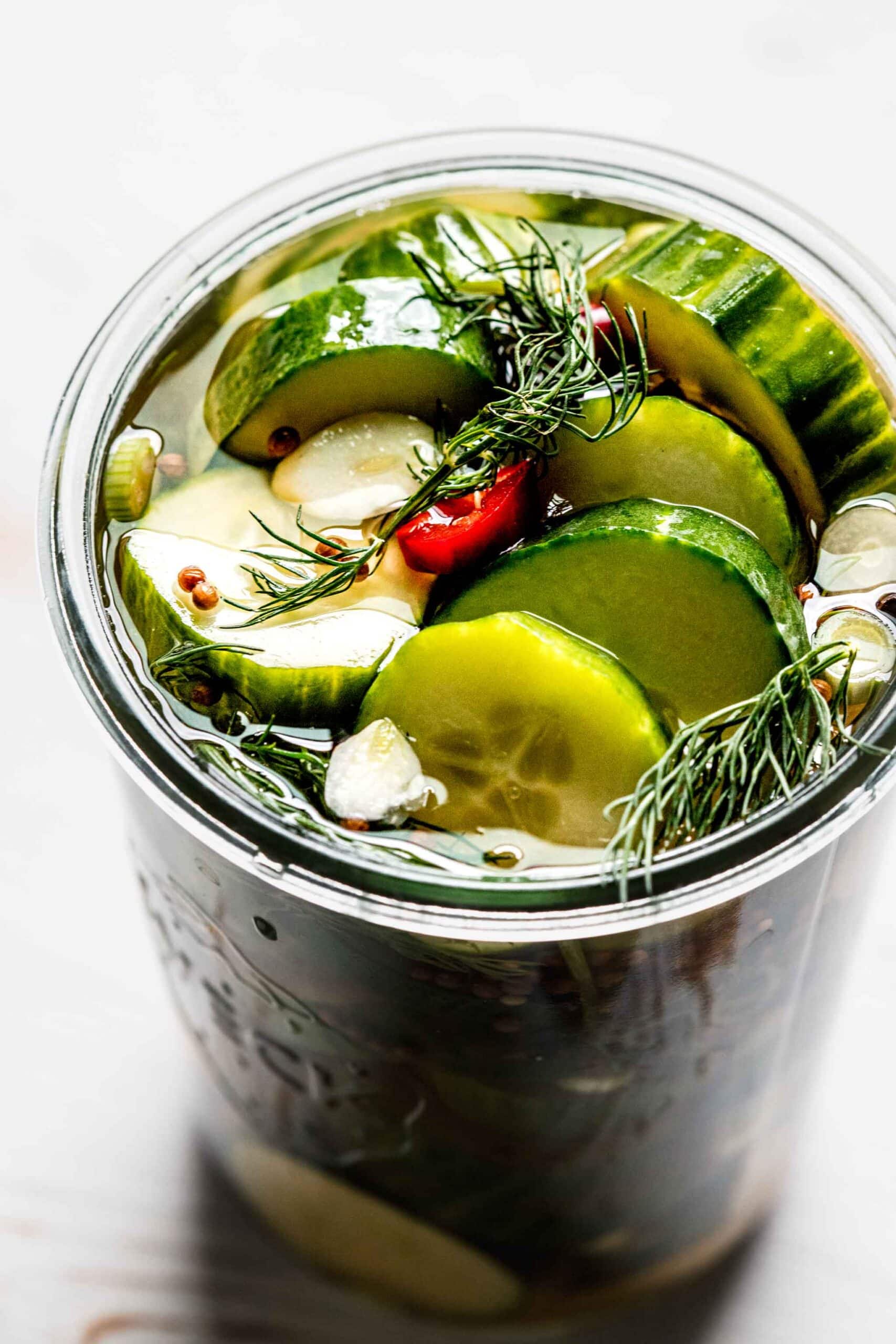 Overhead close up of prepared pickles in weck jar with dill sprigs and red pepper slices.
