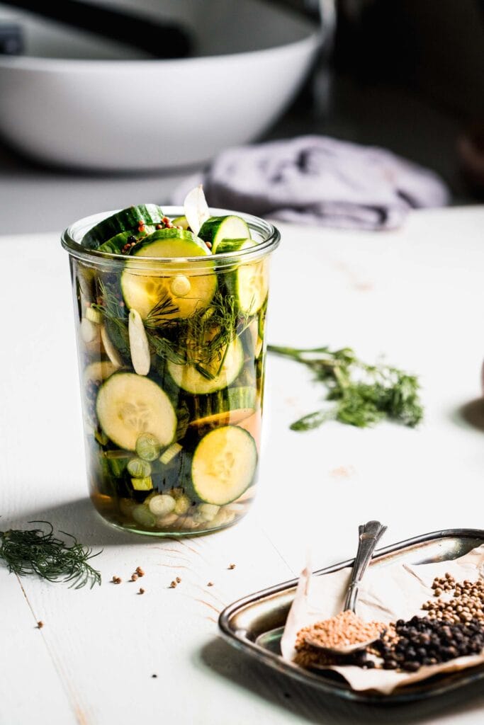 Side view of jar of pickles next to small plate of spices.