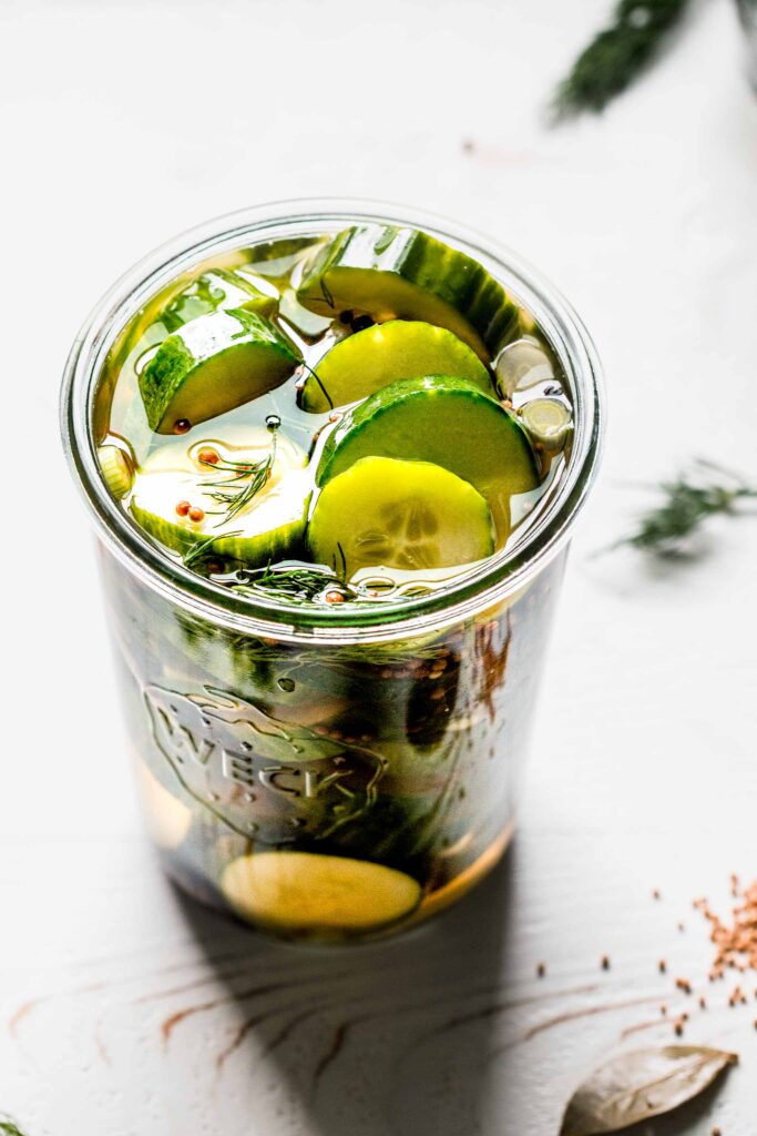 Side view of jar of pickles on white wood counter.