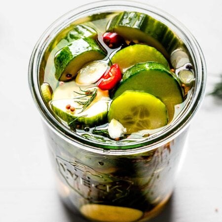 Overhead close up of prepared pickles in weck jar with dill sprigs and red pepper slices.