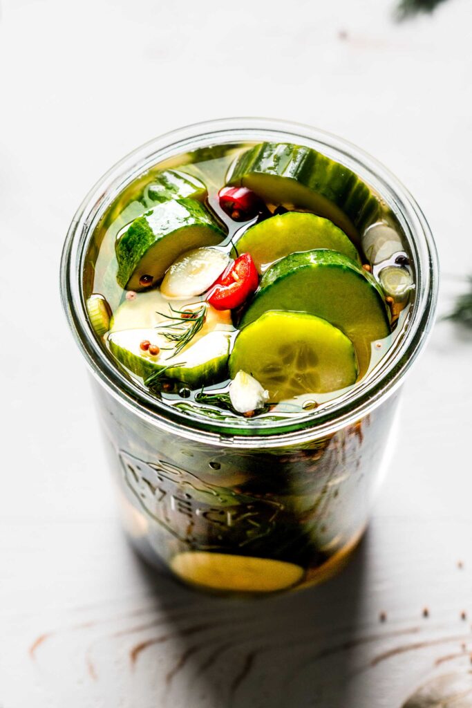 Overhead close up of prepared pickles in weck jar with dill sprigs and red pepper slices.