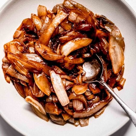 Overhead shot of sauteed onions in white bowl with spoon.