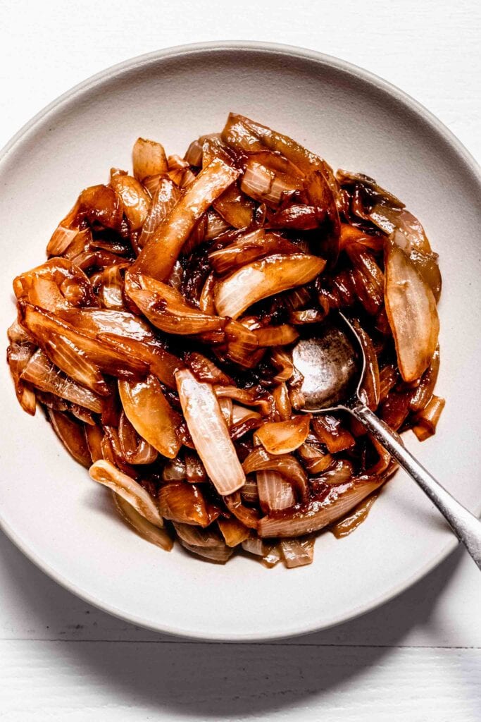 Overhead shot of sauteed onions in white bowl with spoon.